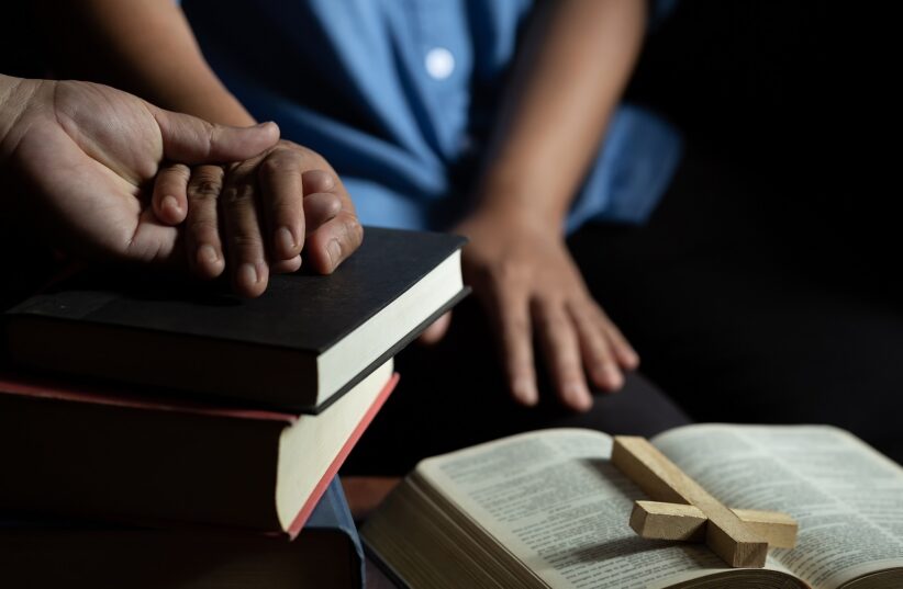 Family group are praying together on wooden table with the light from candle with copy space for your text